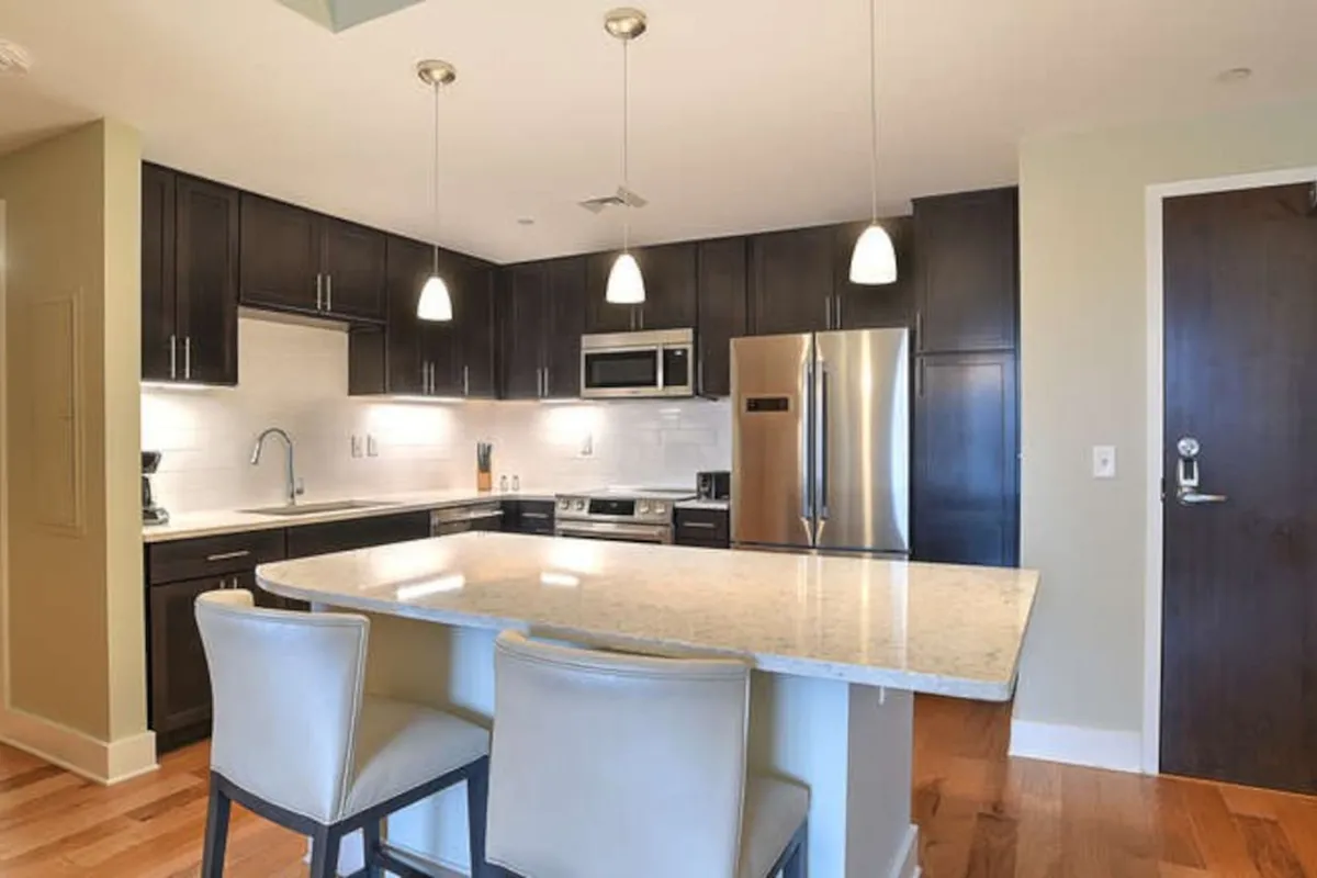 This image features a spacious kitchen with a granite countertop island, sleek stainless steel appliances, and stylish pendant lighting. The setup is ideal for both cooking and entertaining, with ample workspace and modern amenities that invite group meal preparation and gatherings.
