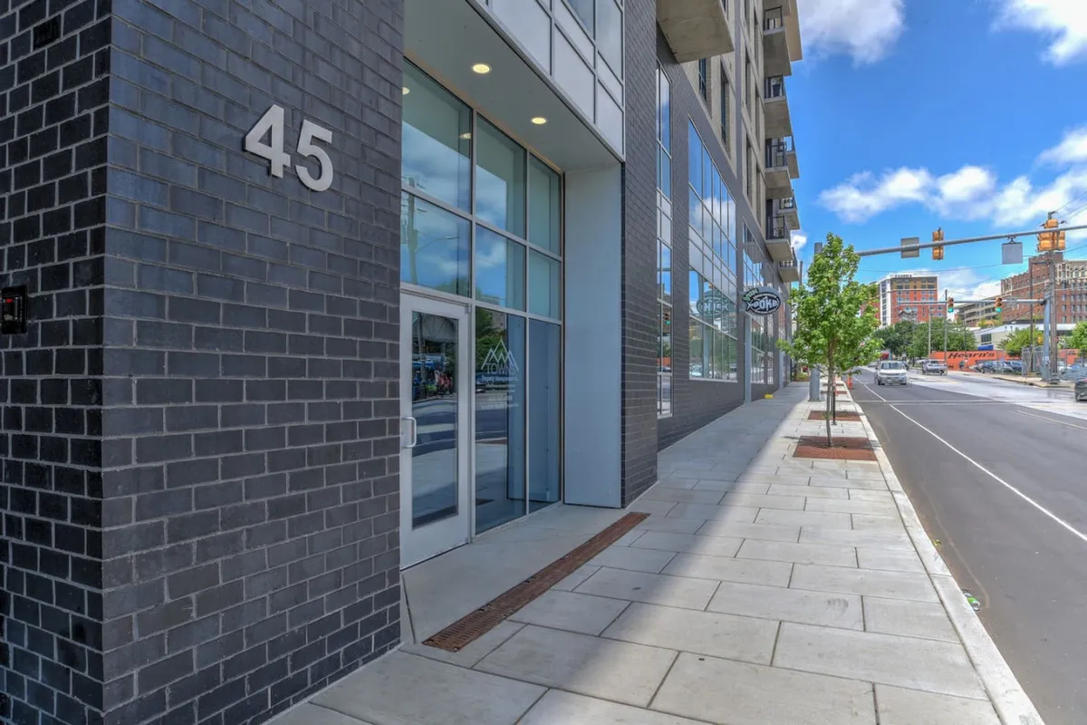 An exterior view of the building entrance, showing the prominent number 45, large windows, and a clean sidewalk leading to the secure doorway. The scene suggests an urban environment and highlights the ease of access from the street.