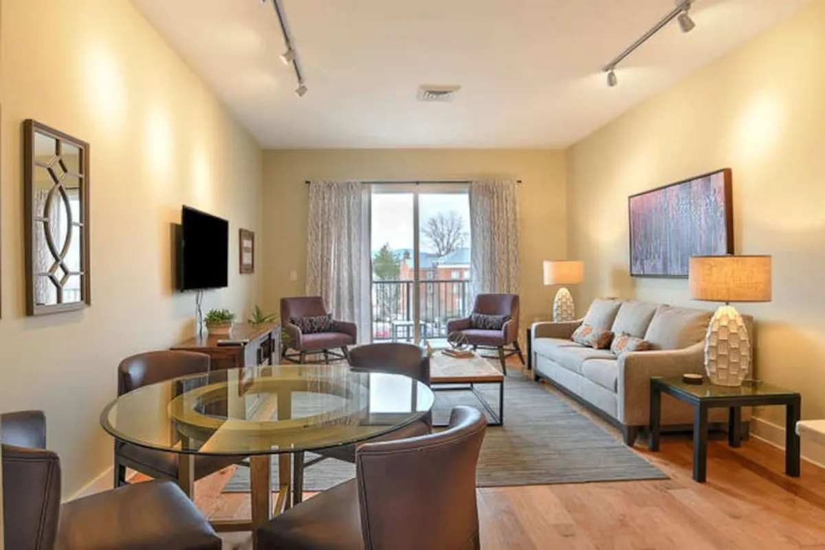 This image features a bright, open-concept living and dining space with a comfortable sofa, a dining table, and expansive windows that fill the room with natural light. The area is arranged for both relaxation and entertaining, embodying an inviting and social atmosphere.