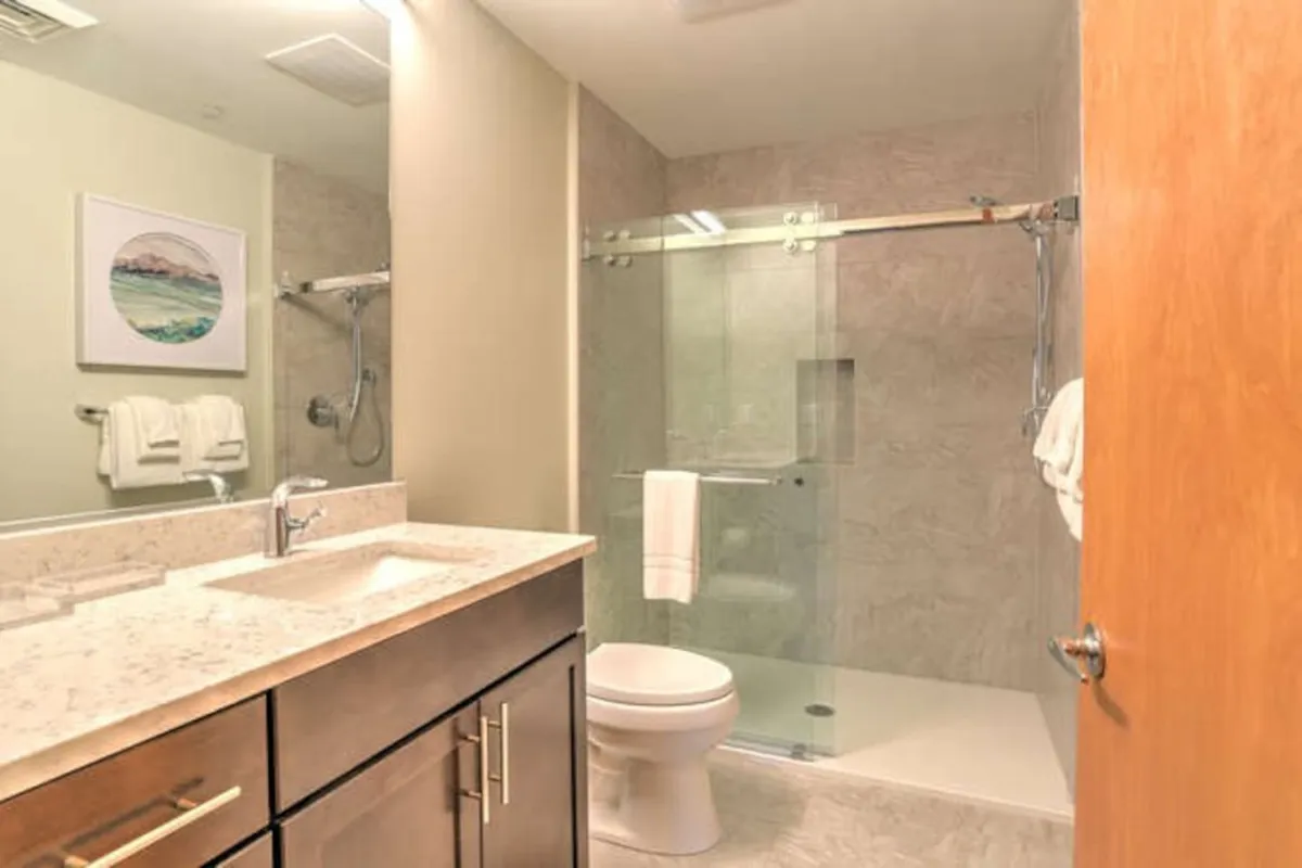 A bright, modern bathroom highlighting a stylish vanity with sink, glass-enclosed shower area, and appealing decorative artwork. The space feels serene and functional, supporting routines like refreshing morning showers or relaxing baths after a day of sightseeing.