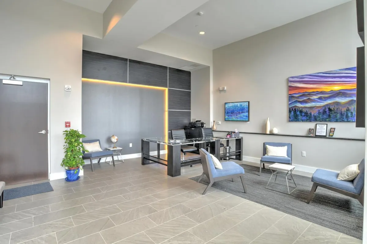 A modern entryway with a sleek desk, comfortable seating, and tasteful artwork on the wall. The space exudes a warm and professional welcome, indicative of a secured building and a thoughtful, accessible entry. The wide doorway and clear, unobstructed pathways reinforce the accessibility features mentioned in the section.